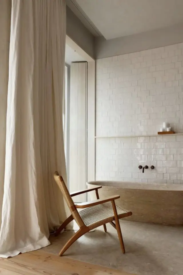 exemple salle de bain minimaliste et cosy baignoire îlot pierre carrelage murale blanc grand rideau couleur beige fauteuil petite étagère murale bois