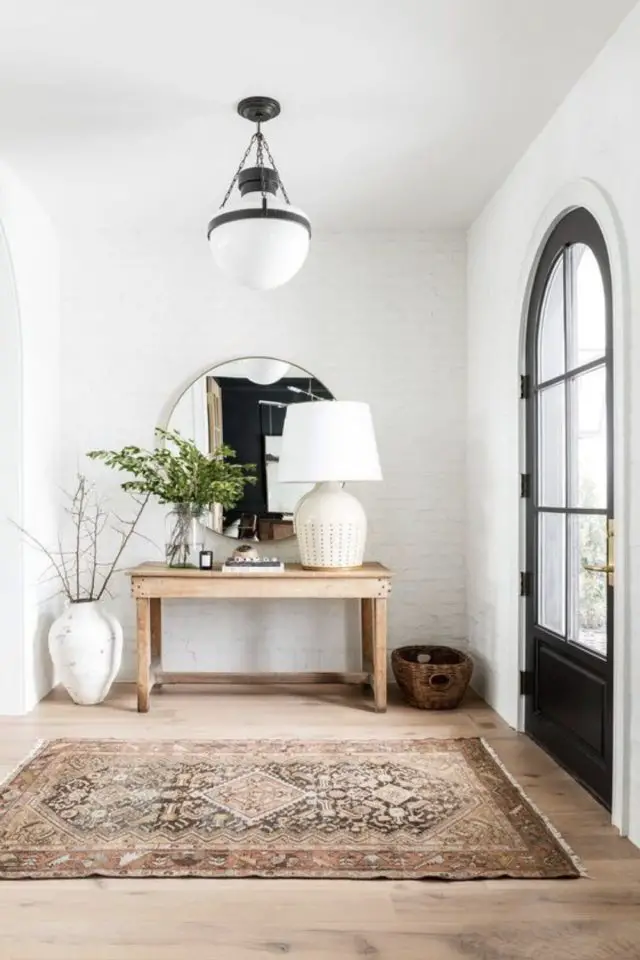 decor entree console exemple style slow living chic meuble en bois parquet grand tapis oriental miroir rond vase et lampe à poser blanche espace lumineux à côté de la porte d'entrée