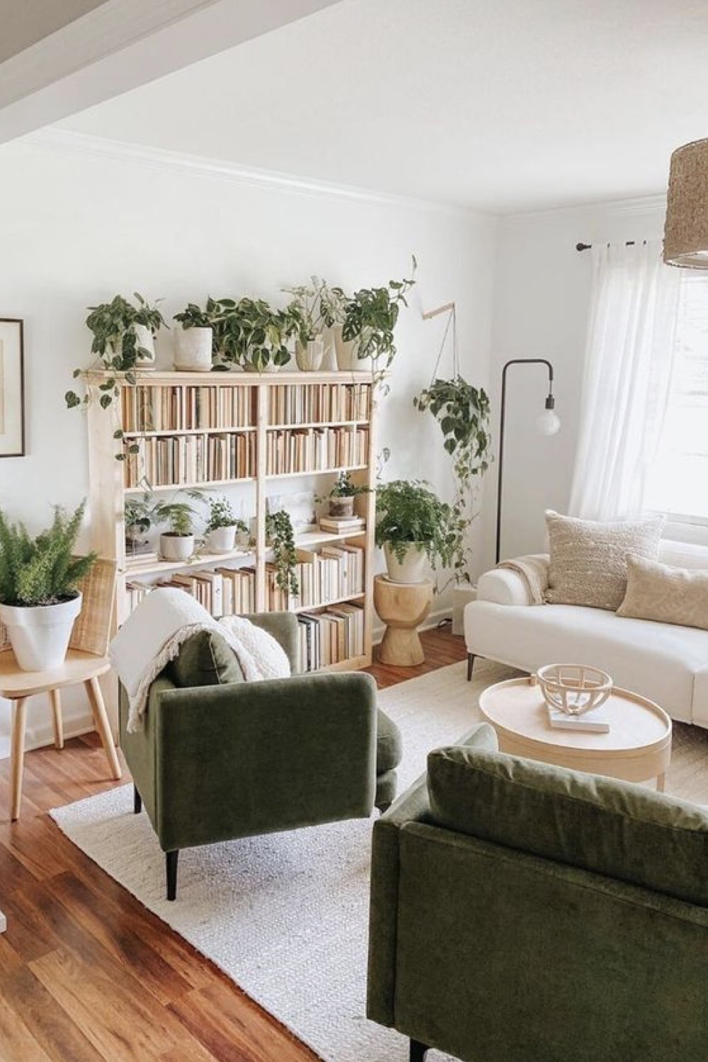 decoration salon tendance 2023 bibliothèque en bois clair plantes vertes fauteuil vert canapé blanc tapis neutre pièce à vivre lumineuse
