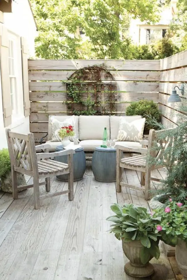 amenagement deco petit patio exterieur clôture brise-vue en bois cosy intime et chaleureux revêtement terrasse sol bois vieilli petite banquette table basse double fauteuil modulable