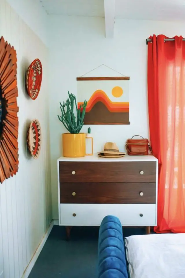 interieur vintage caracteristique decor chambre à coucher adulte années 70 seventies commode blanche et bois sombre affiche poster déco orange marron et jaune rideaux coloré
