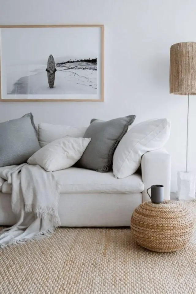 caracteristique decor bord de mer salon séjour couleur neutre canapé blanc coussin gris tableau poster photo paysage tapis naturel en jute pouf