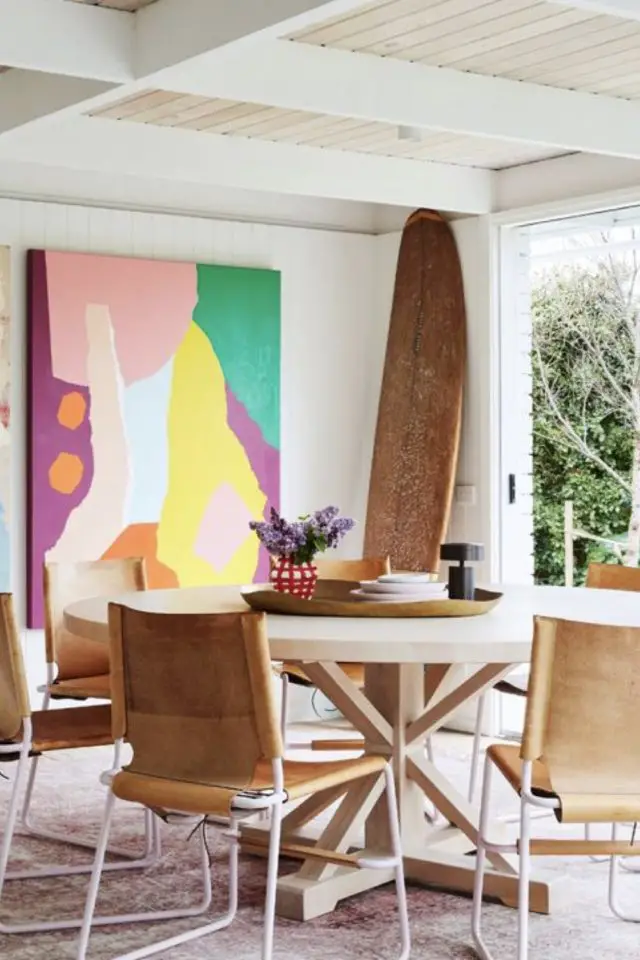 caracteristique decor bord de mer salle à manger coin repas table ronde blanche fauteuil en cuir chic grand tableau coloré planche de surf