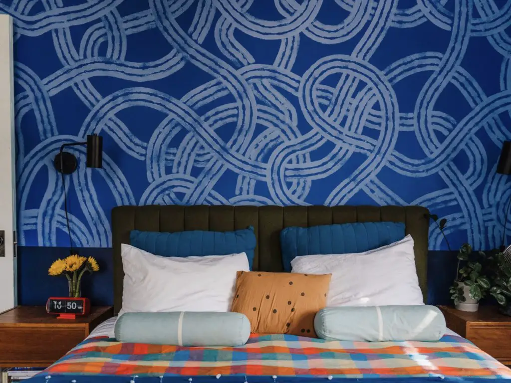decor maison couleur joyeuse famille chambre à coucher adulte mur accent bleu avec motif plus clair tête de lit sombre linge dépareillé beaucoup de personnalité