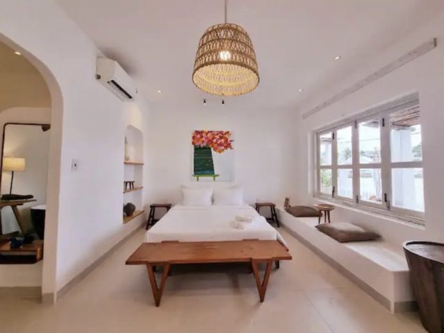 villa style mediterraneen voyage asie sud-est chambre à coucher blanche simple lit deux personnes luminaire en rotin tableau coloré bout de lit en bois