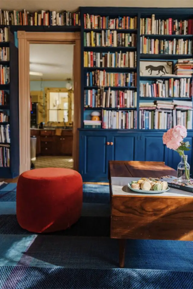 visite deco maison hyper coloree et joyeuse grande bibliothèque peinte en bleu pouf en velours orange tapis XXL coloré