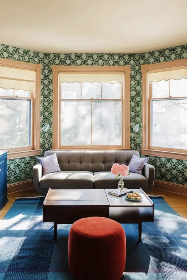 visite deco maison hyper coloree et joyeuse salon séjour petit canapé gris revêtement mural papier peint à motif tapis bleu pouf orange table basse en bois vintage