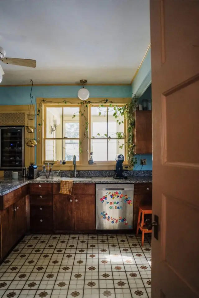 visite deco maison hyper coloree et joyeuse cuisine vintage rétro sol à motif vintage meuble en bois encadrement fenêtre jaune et mur bleu vert plantes