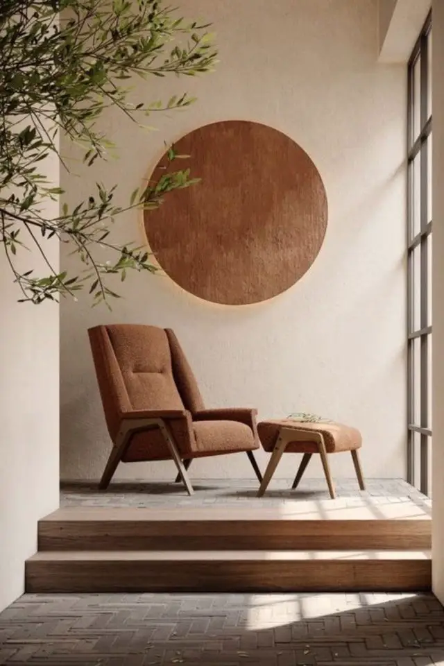 decor wabi sabi caracteristiques coin tranquille en face d'une baie vitrée fauteuil vintage marron avec repose-pied grande applique murale ronde décorative couleur neutre et organique