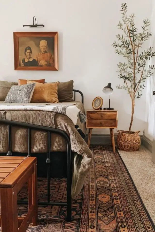 chambre a coucher cocooning moderne bohème chic tapis oriental lit noir couleur chaude parure de lit petit arbuste angle de la pièce table de nuit en bois
