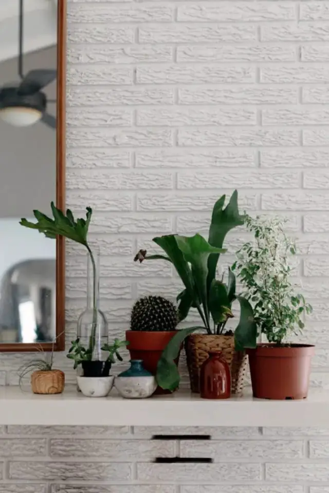 visite maison deco boheme retro chic ensemble de plantes vertes posées sur la cheminée du salon mur en brique blanche