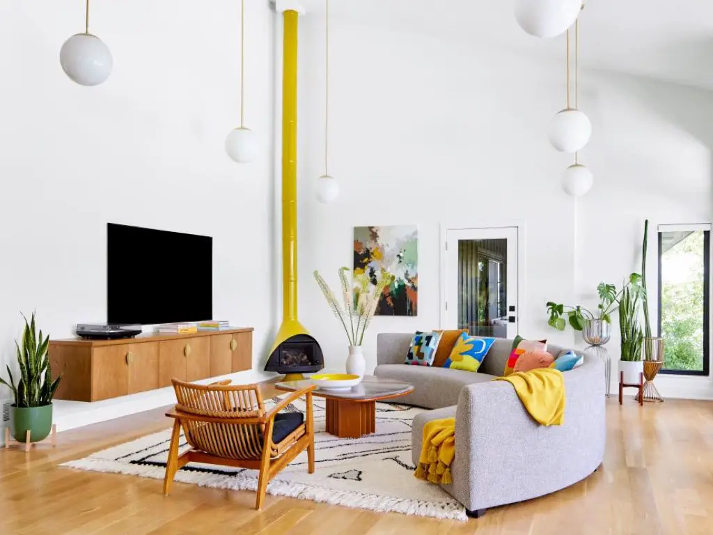 visite maison renovation mid century modern salon séjour grande pièce blanche cheminée design jaune meuble TV mural en bois canapé arrondi tapis banc et noir fauteuil bas