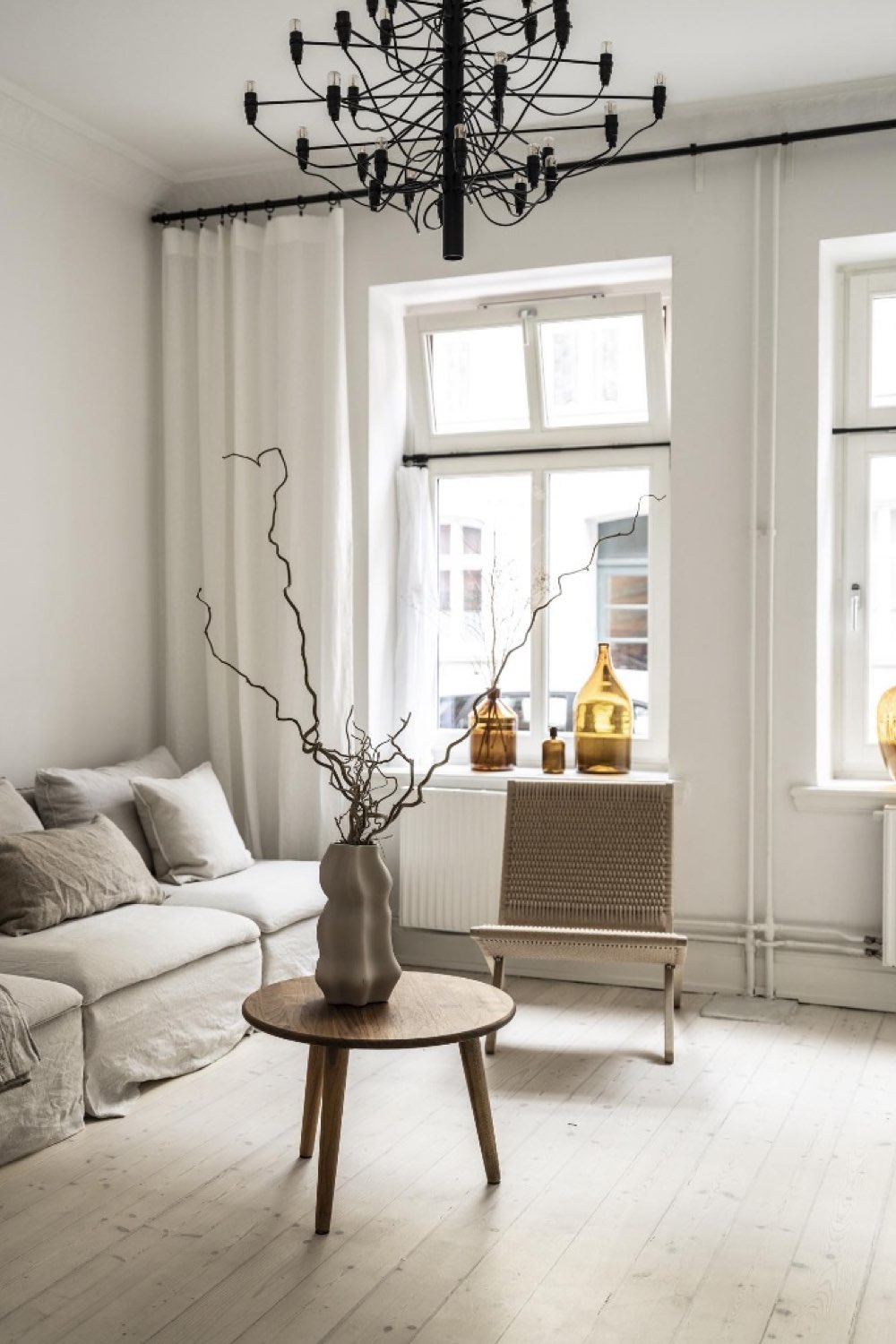 decor maison minimaliste et cosy simple épuré salon séjour canapé familial table basse ronde en bois grande fenêtre rideaux ton sur ton mur
