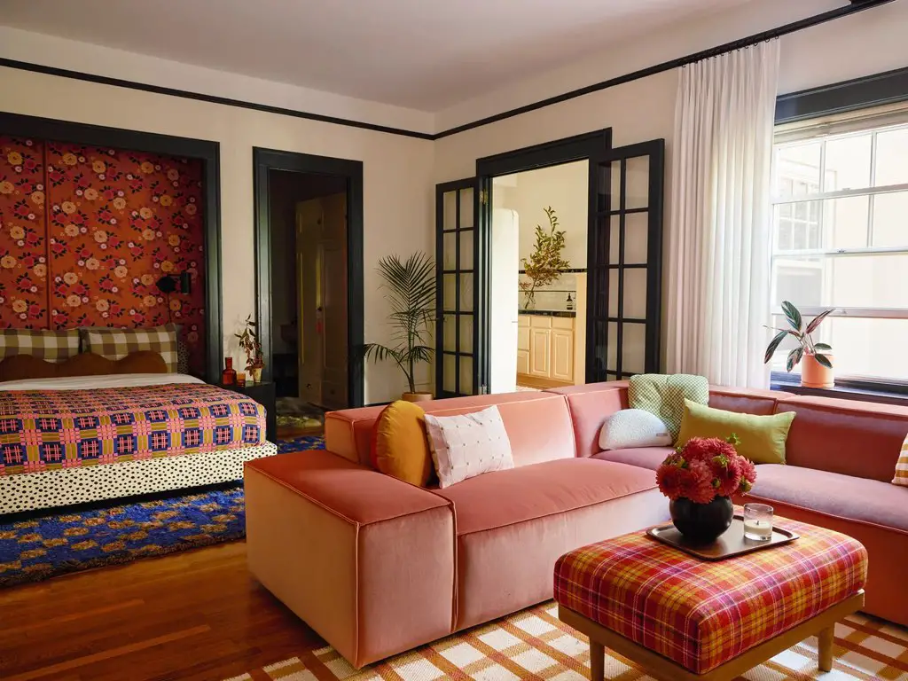 visite deco appartement colore motif eclectique studio salon et chambre canapé rose tapis à carreaux pouf table de basse tartan papier peint floral
