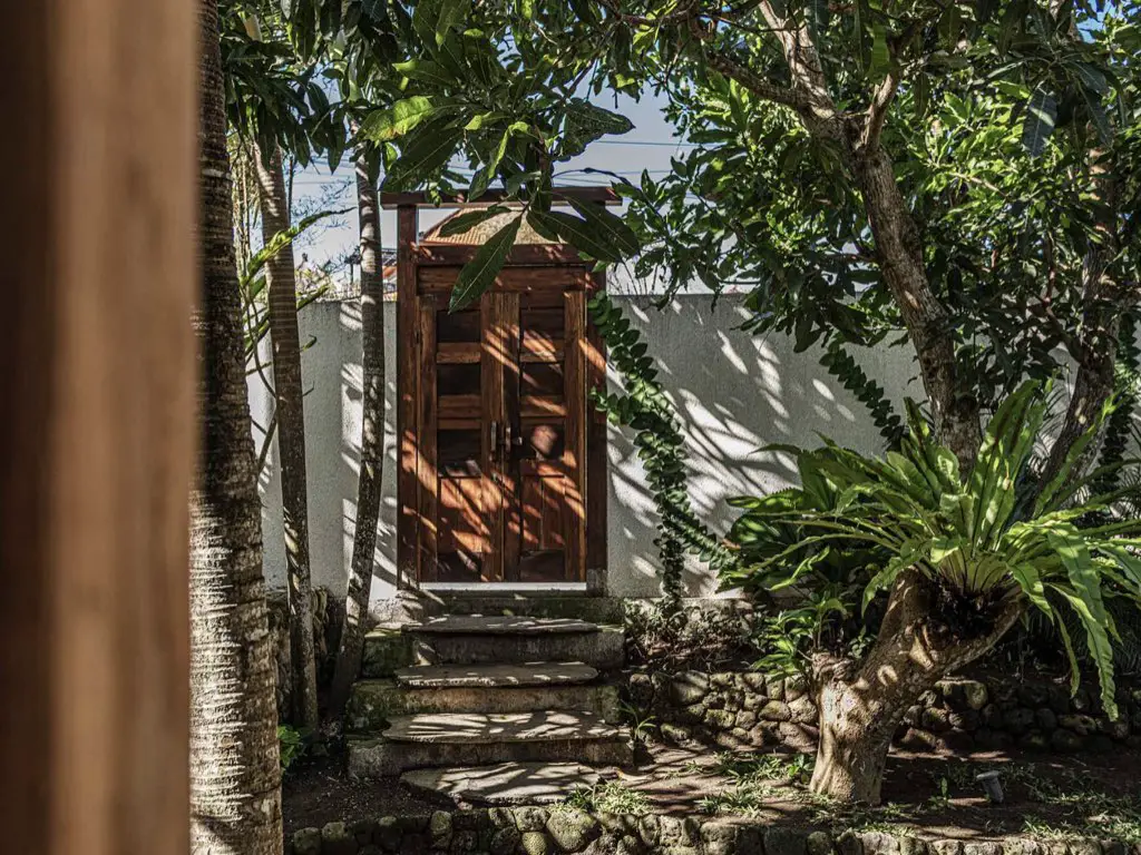maison ouverte sur exterieur nature jardin tropical porte en bois mur blanc allée en pierre