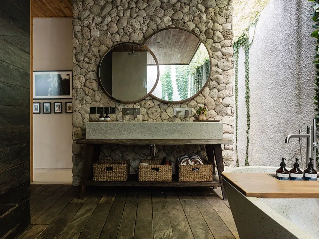 maison ouverte sur exterieur nature grande salle de bain mur en pierre miroir rond grande vasque en béton