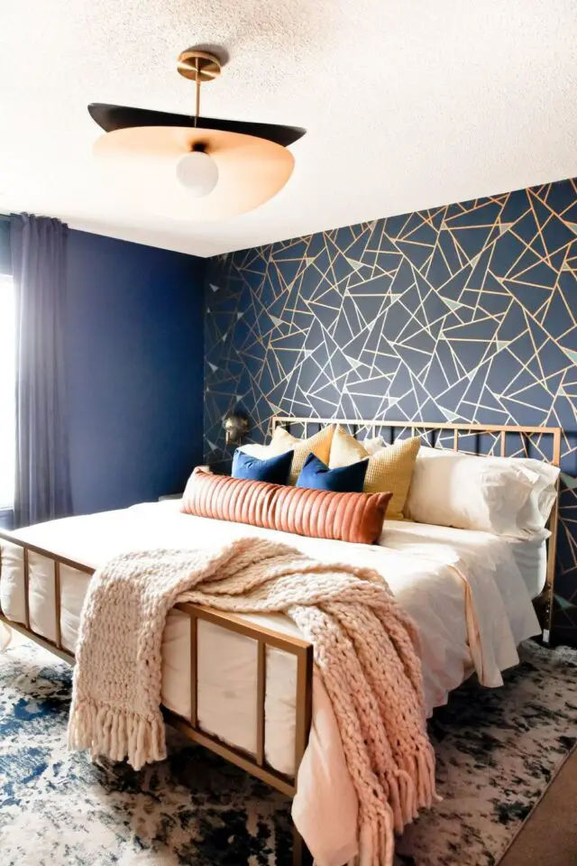 decoration coloree exuberante et audacieuse chambre à coucher parentale couleur sourde bleu nuit mur accent papier peint géométrique bleu et or cadre de lit en laiton