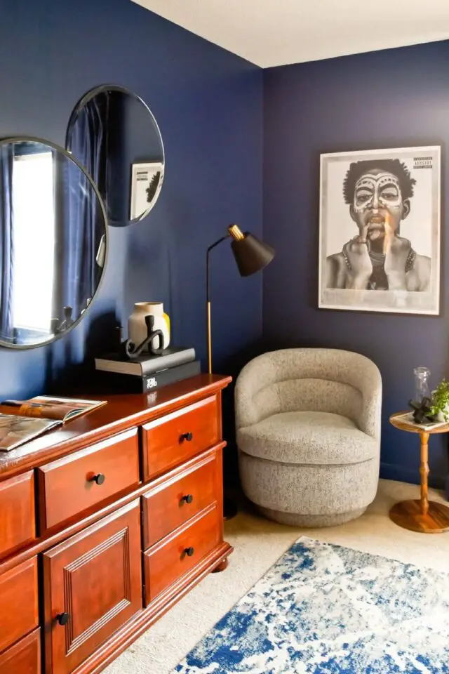 decoration coloree exuberante et audacieuse chambre à coucher parentale peinture bleu nuit commode en bois miroir rond lampadaire noir affiche photo encadrée noir et blanc