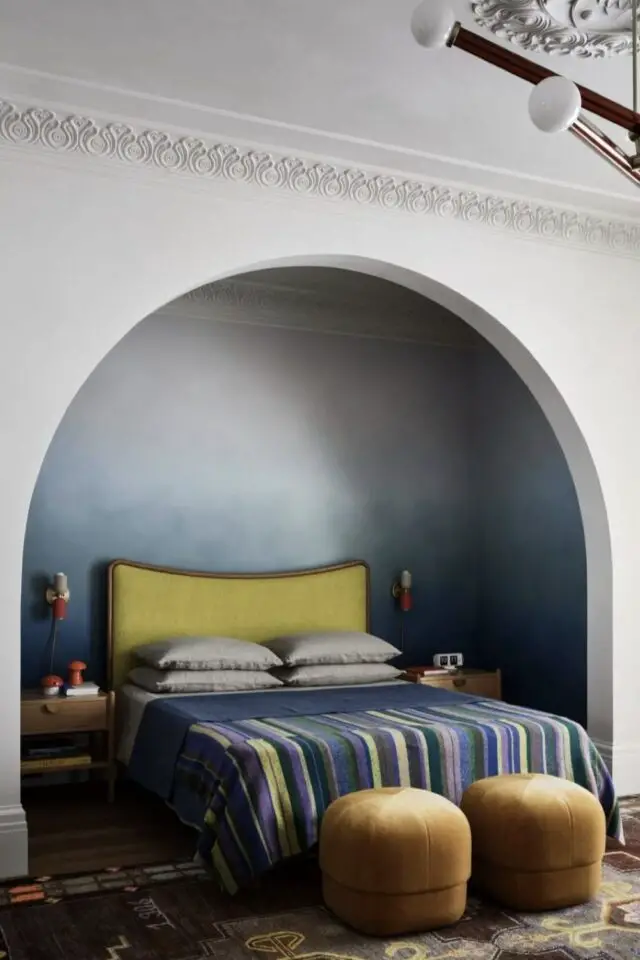 alcôve chambre décoration grand renfoncement arche moulure haut du mur papier peint dégradé de bleu tye and dye tâte de lit jaune table de chevet en bois deux poufs en bout de lit 