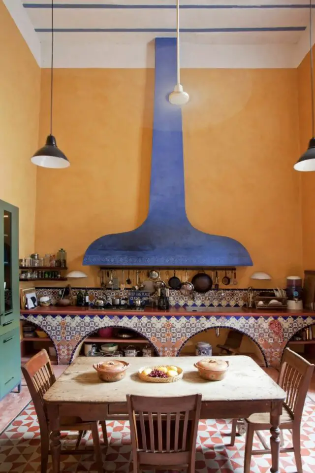cuisine ambiance mexicaine décoration mur jaune hotte bleu cobalt meuble avec niche revêtement carrelé table en bois chaise ancienne sol motif blanc et terracotta meuble vitrine vert 