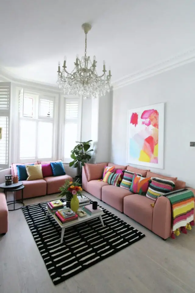 jolie décoration de salon photo séjour appartement mur blanc lumineux tapis noir et blanc canapés roses avec coussins multicolores lustre à pampilles tableau abstrait 