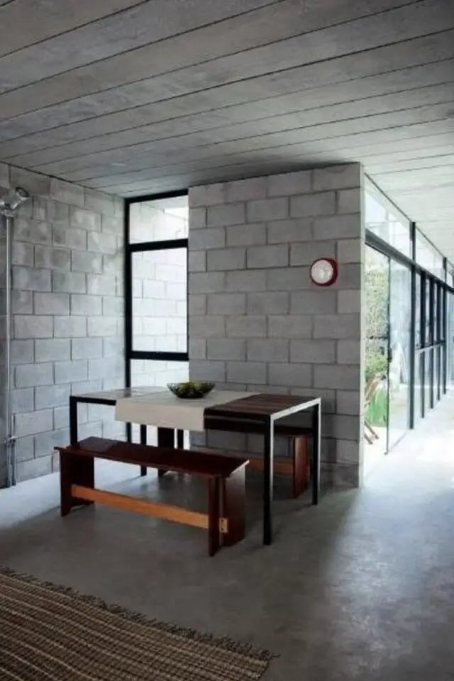 mur intérieur en parpaings bruts espace salle à manger épuré sol en béton ciré table et banc bois sombre baie vitrée menuiserie aluminium noir mur intérieur en parpaings bruts espace salle à manger épuré sol en béton ciré table et banc bois sombre baie vitrée menuiserie aluminium noir