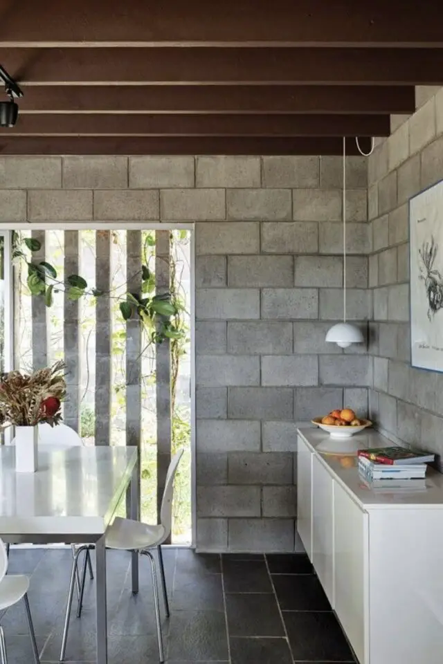 mur intérieur en parpaings bruts salle à manger poutre plafond meuble blanc table laquée blanche brise-vues extérieur plantes grimpante sol carrelage noir mur intérieur en parpaings bruts salle à manger poutre plafond meuble blanc table laquée blanche brise-vues extérieur plantes grimpante sol carrelage noir