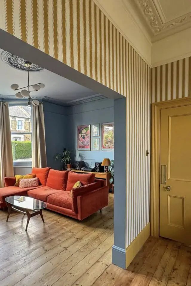 décoration couleur jaune et bleu salon salle à manger séparé par une arche ouverte espace séjour bleu canapé orange espace repas papier peint rayé jaune et blanc peinture porte en bois et plinthe 