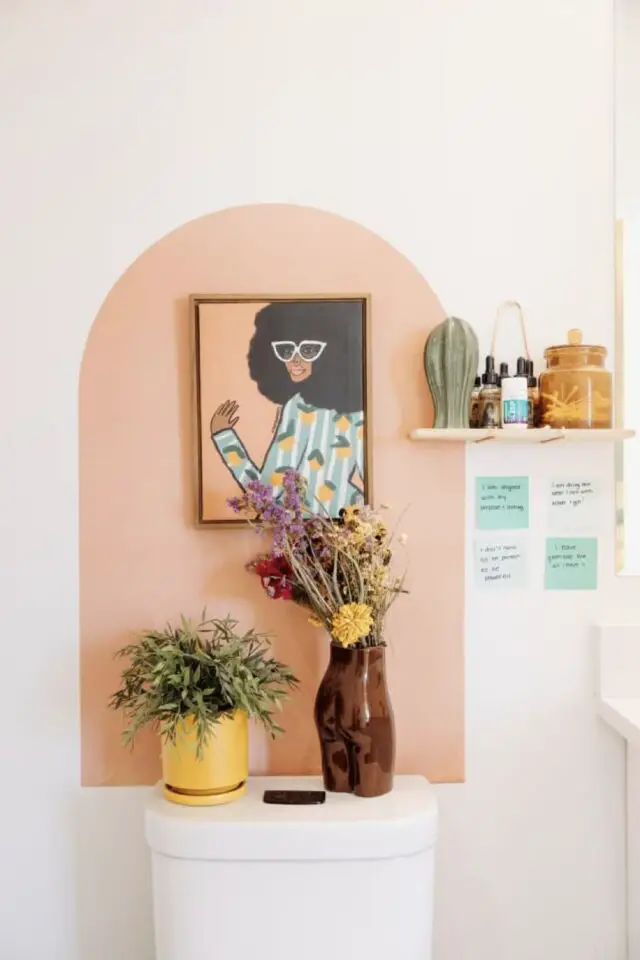dessus du réservoir des toilettes arche en peinture couleur corail avec poster encadré harmonie de couleur petite étagères en bois décoration murale salle de bain idée à copier 