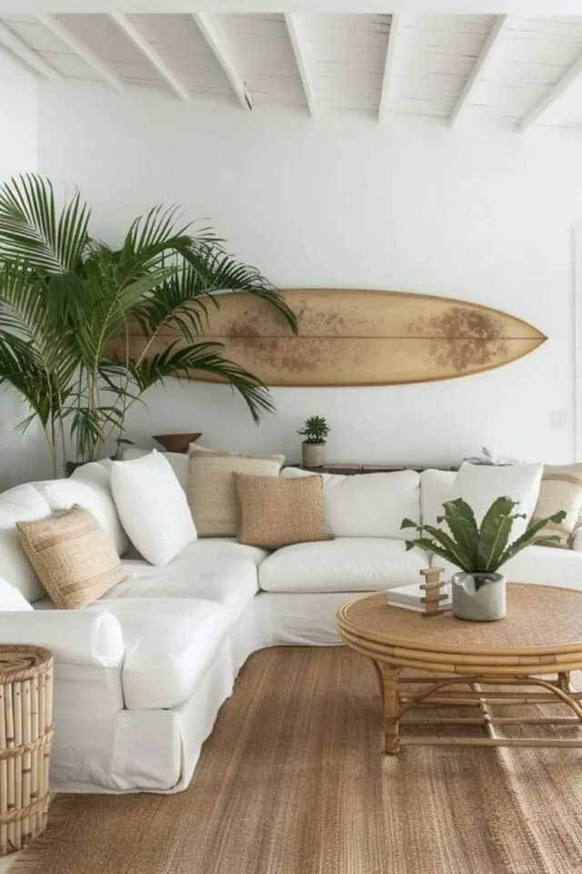 décoration bord de mer salon blanc et neutre coussin beige tapis jonc de mer planche de surf accrochée au mur table basse vintage en rotin 
