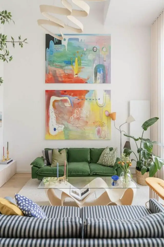 salon moderne et design avec une grande hauteur sous plafond grands tableaux colorés abstraits au dessus du canapé table basse design avec plateau en verre 