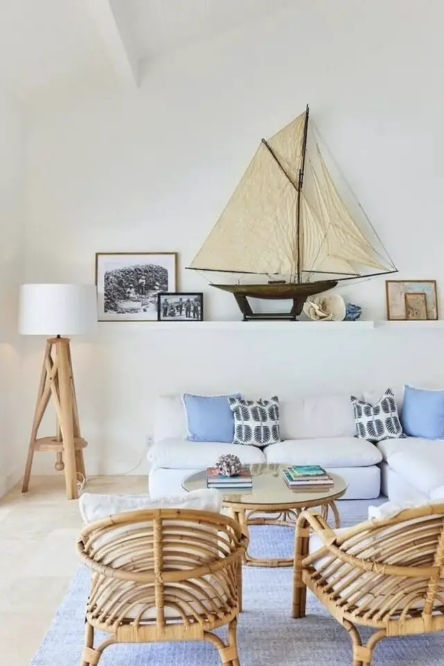salon style bord de mer moderne mur beige presque blanc accessoires décoratifs tapis coussins pour une touche de bleu fauteuil en rotin lampe bois flotté objet bateau à voile 