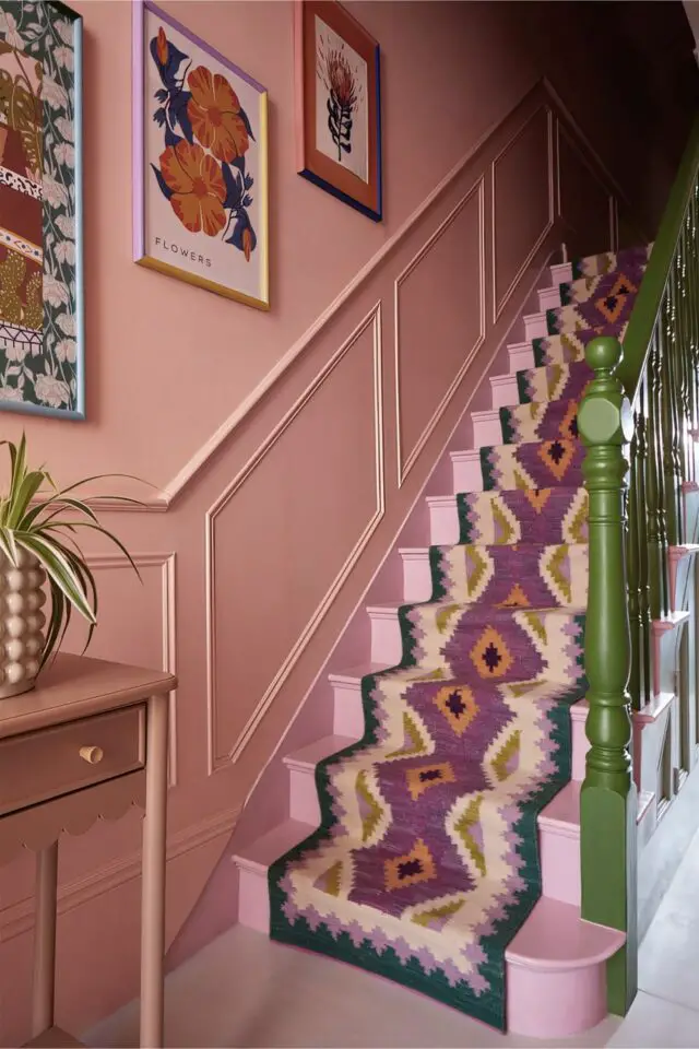 cage d'escalier déco whimsical peinture vieux rose sur les marches moulures et mur tapis à motifs et illustrations encadrées rampe peinte en vert contraste couleur complémentaire 