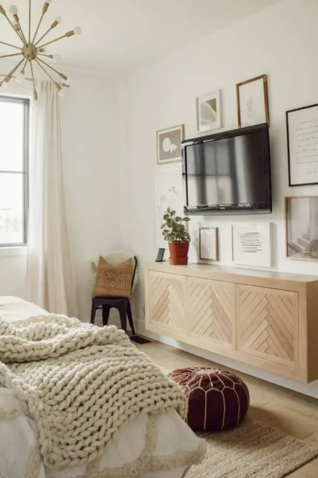 Mur Tv moderne chambre adulte blanche écran accroché au dessus d'un meuble mural en bois galerie de cadres petite plante verte 