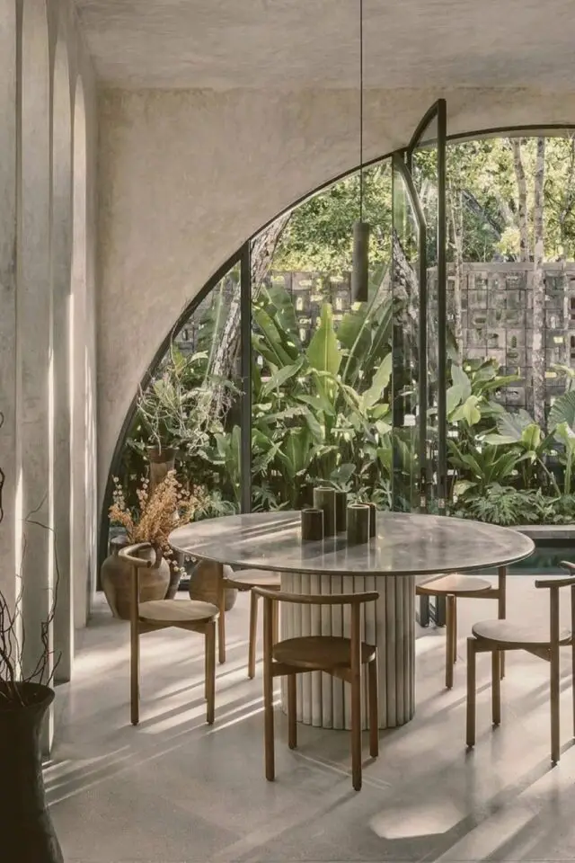 salle à manger table ronde en marbre pied central moderne cannelé chaise en bois grande baie vitrée cintrée vue sur jardin tropical 