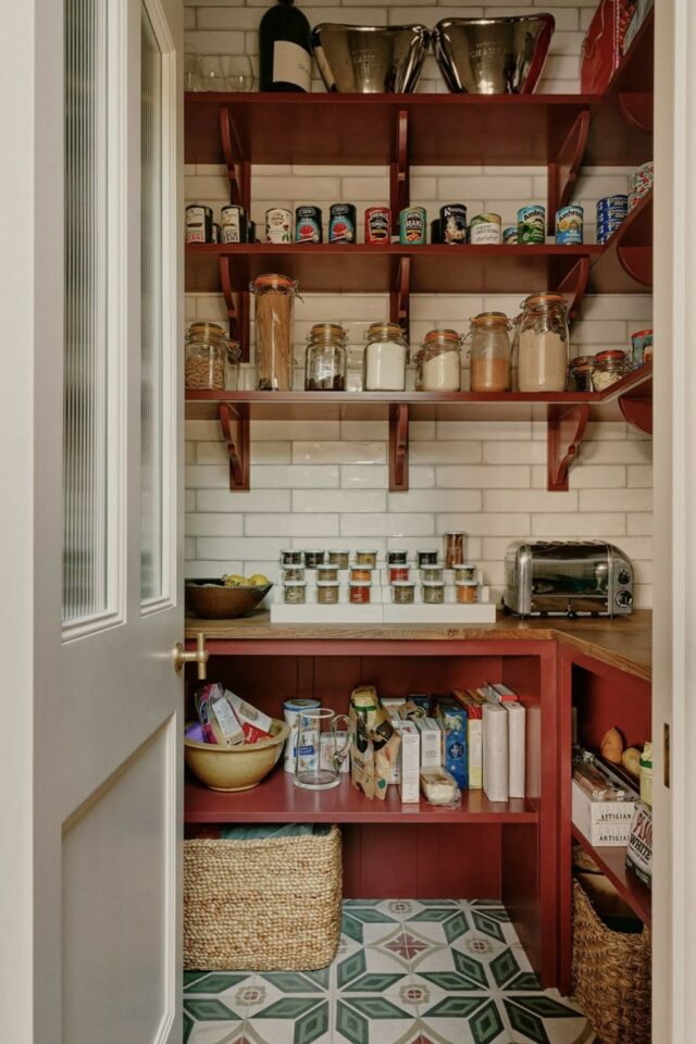 arrière-cuisine aménagée avec livres de cuisine rangés en bas bocaux à épices sur le plan de travail à côté du grille-pain et étagères avec boaux et boite de conserve 